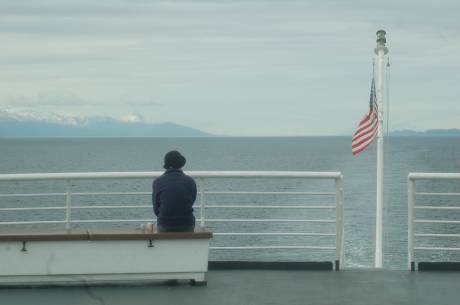lone passenger looking out to water at back of ship